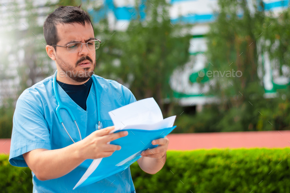 young caucasian male doctor with a beard with a worried face reading a medical record