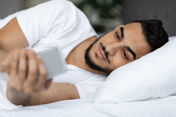 Gadget Addiction. Arab Guy Browsing Internet On Smartphone While Lying In Bed