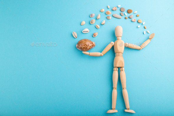 Wooden mannequin juggling sea shells on blue pastel background. copy space.