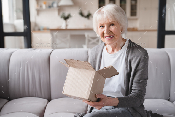 Grandmother opening receiving post parcel delivery presents gifts, ordering goods online on Internet