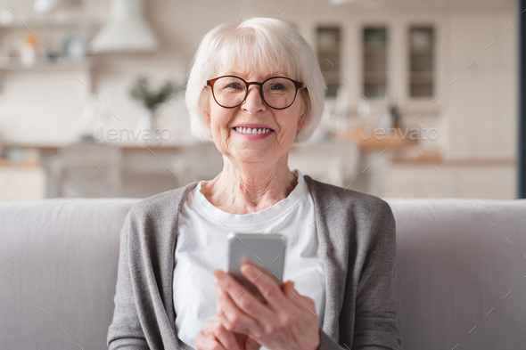 Grandmother using smartphone cellphone for e-banking e-commerce, surfing social media online at home