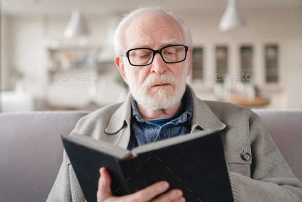 Grandfather reading book wearing glasses, learning remotely, literature ...