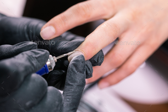 Hardware manicure in a beauty salon. Female manicurist is applying electric nail file drill to