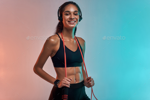 Music is my motivation. Sporty young woman in headphones holding jumping rope on shoulders and