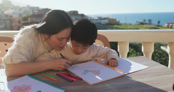Asian mother doing homework with his little son outdoor on sunny day alt