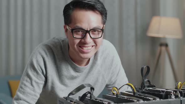 Close Up Of Asian Man Smiling To Camera While Using Laptop And Mining Rig For Mining Cryptocurrency alt