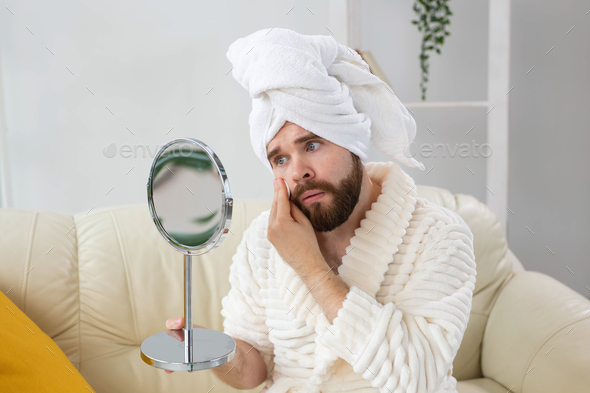 Handsome man cleaning face skin with batting cotton pads and looking at mirror. Spa, body and skin