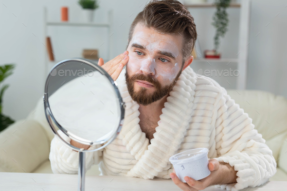 Bearded guy applying anti-wrinkle cream on his face. Skin care and spa for man concept