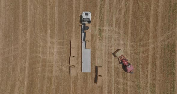 Red tractor loading Hay bales onto a parked truck, Aerial footage. alt