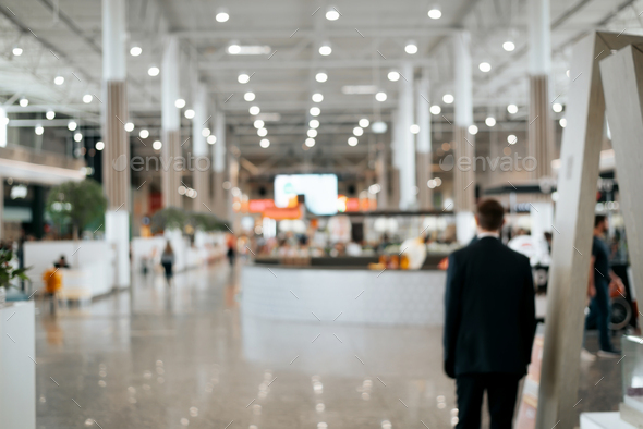 Defocused shopping mall background, large illuminated hall, security guard rear view. Blurred