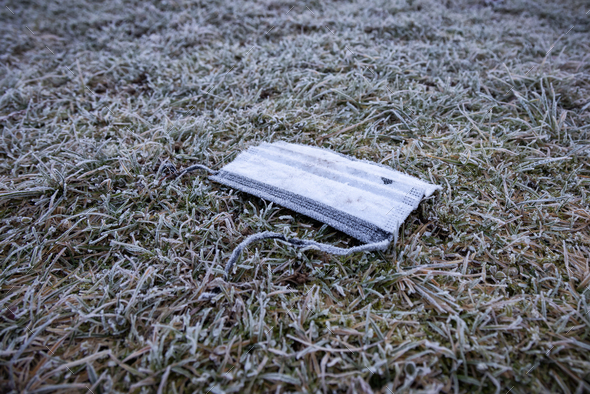 Face mask garbage on the ground. frosty grass in winter season