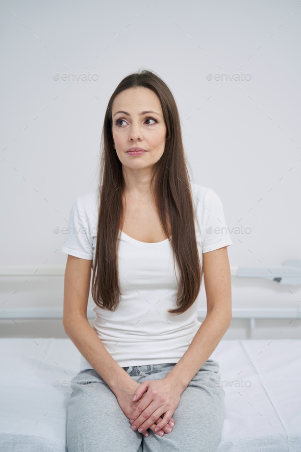 Low-spirited young woman sitting in hospital ward