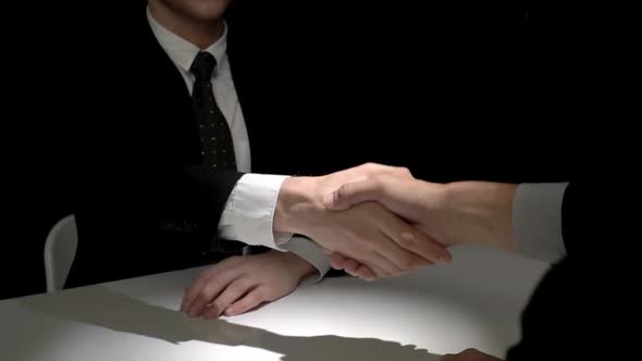 Two businessmen making handshake in dark room after negotiation for illegal deal