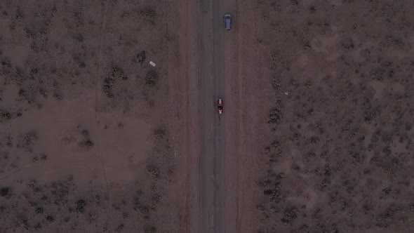 AERIAL: Birds View Flight Over Lonely Abandoned Desert Road with Red Car Driving in the Distance  alt