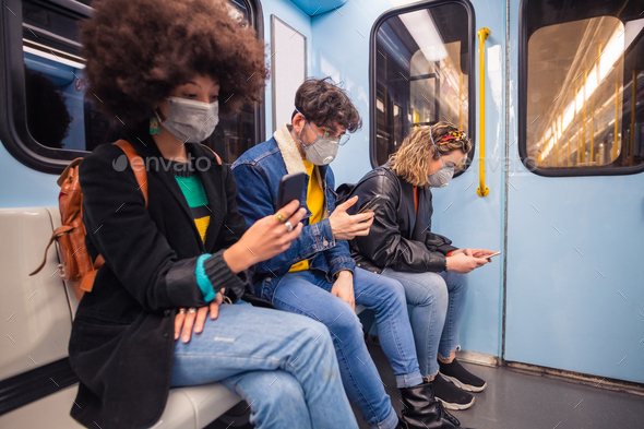 Multiethnic friends wearing medical mask in the subway using smartphone