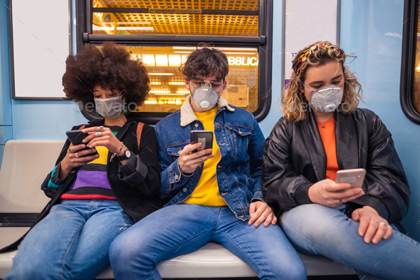 multiethnic friends wearing medical mask in the subway using smartphone