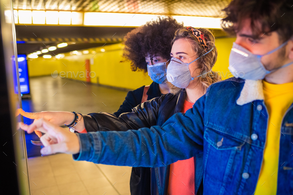 Three multiethnic friends wearing medical mask protecting from pollution and virus using touchscreen