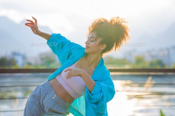 mixed race curly woman enjoying dance at sunset in beach