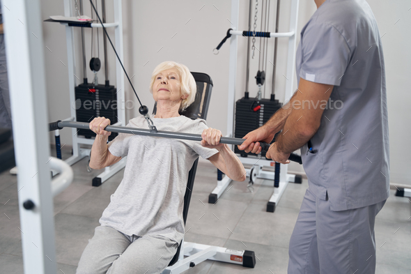 Old lady pulling weight on training equipment with hands Stock