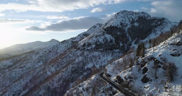Backward Aerial Top View Along Road on White Snow Mountain in Winter