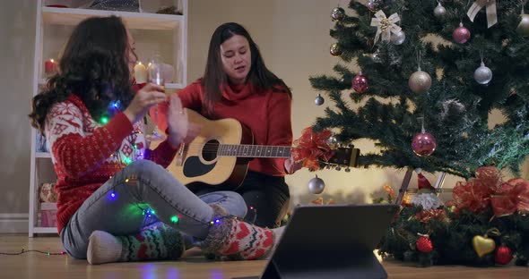 Talented Caucasian Musician Playing Guitar Singing with Friend Sitting at Christmas Tree Indoors alt