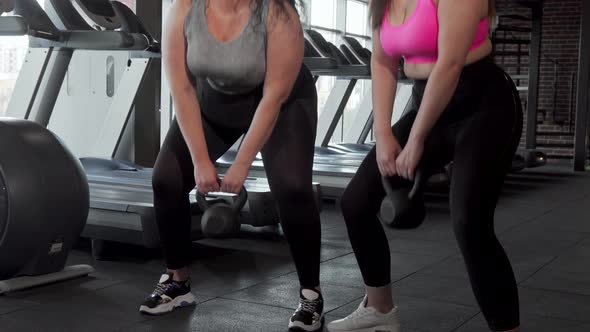 Sliding Shot of Two Plus Size Sportswomen Exercising with Kettlebell at the Gym