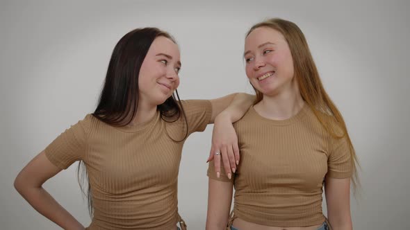 Relaxed Confident Twin Sisters Posing at Grey Background Looking at Camera Laughing alt