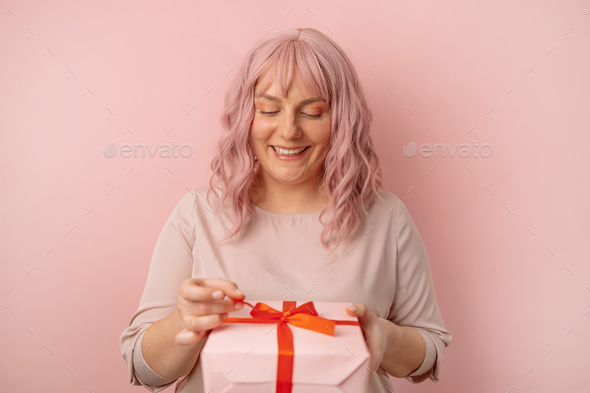 Happy young pink hair woman holding present gift box with red ribbon bow posing