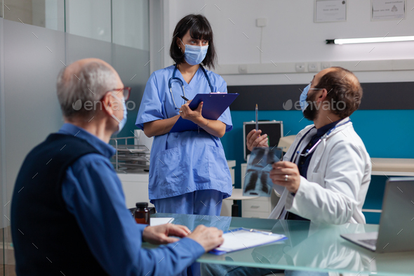 Physician Talking To Nurse And Holding X Ray Scan At Checkup Visit ...