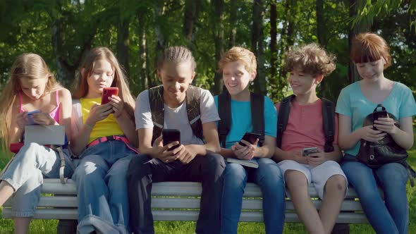 Multiethnic Teen Kids with Mobile Phone Sitting on Bench Outdoors alt