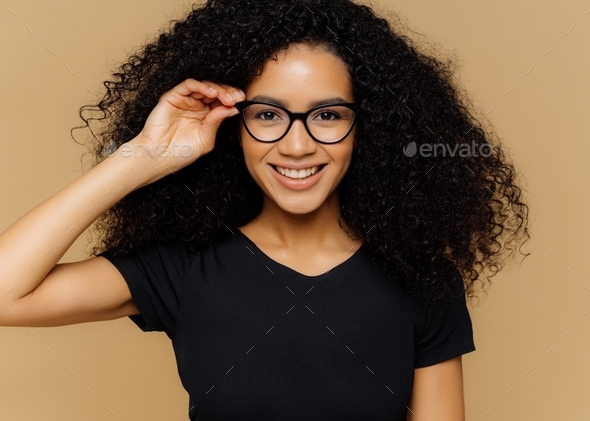 African American woman grins at camera, keeps hand on rim of spectacles, glad to hear good news