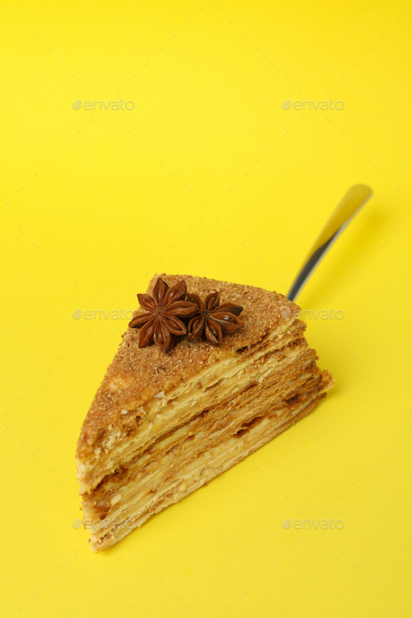 Spatula with piece of honey cake on yellow background