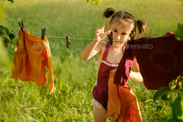 The girl reaches out with her hand to the clothespin to hang clothes to dry