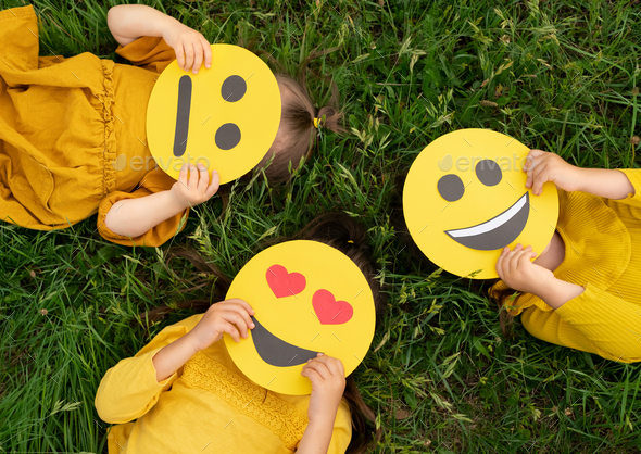 Three children lying on the grass are holding cardboard emoticons - Stock Photo - Images