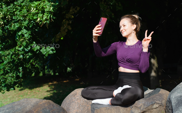 Fit smiling young woman taking selfie on phone during yoga and meditation while sitting in lotus