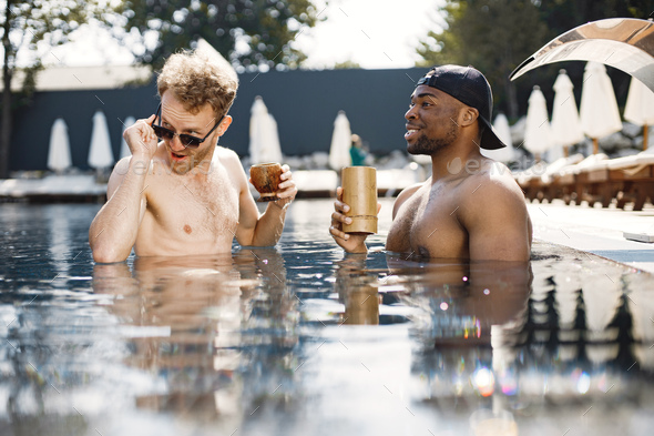 Two male friends relaxing with a cocktails in a swimming pool