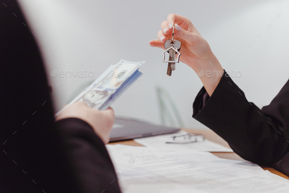 Young woman realtor holds out the keys to the real estate, the client give money
