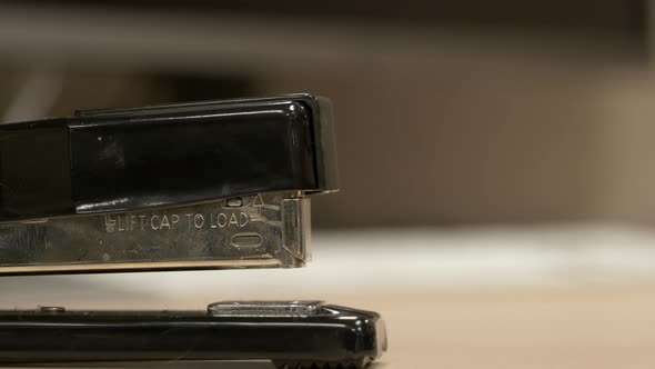 A close up from the side of a black stapler stapling pieces of paper together in slow motion. alt