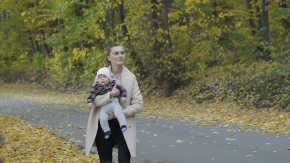 Happy Mother Holds Her Little Baby Son in Embraces Smiling and Walking at Park alt