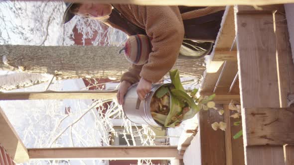 VERTICAL - a mother with child in sling empties compost bucket in a snowy scene alt