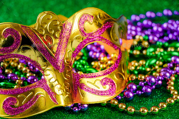 Carnival mask and colorful beads on green shiny background. Mardi Gras concept. Fat Tuesday symbol.