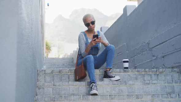 Mixed race woman using smartphone on staircase alt