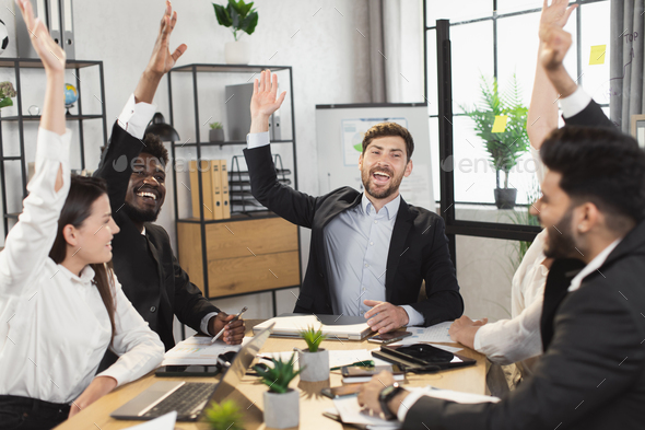 Happy diverse people raising hands during meeting at office