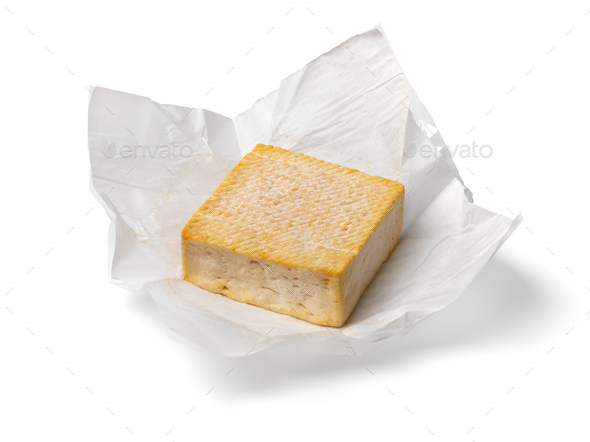 Single whole piece of Limburger or Herve cheese on paper on white background