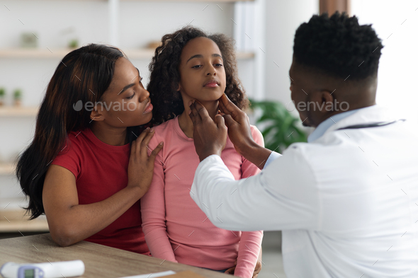 Black doctor palpating school girl throat at clinic