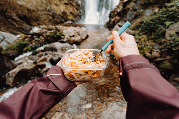 A point of view shot of a female hiker eating in front of a waterfall