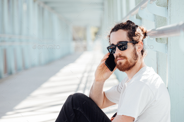 Young hipster man at the airport or bus station waiting while calls someone with the phone