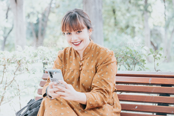 Young woman using smart phone in the city and sitting on the bench during an autumnal
