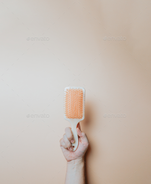 Minimal image of a hand holding an hair comb over a light color background, copy space