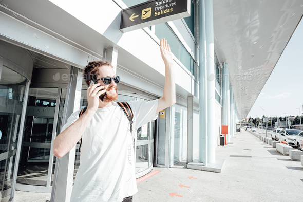 Handsome young hipster man with street clothes talking on phone near airport when arriving